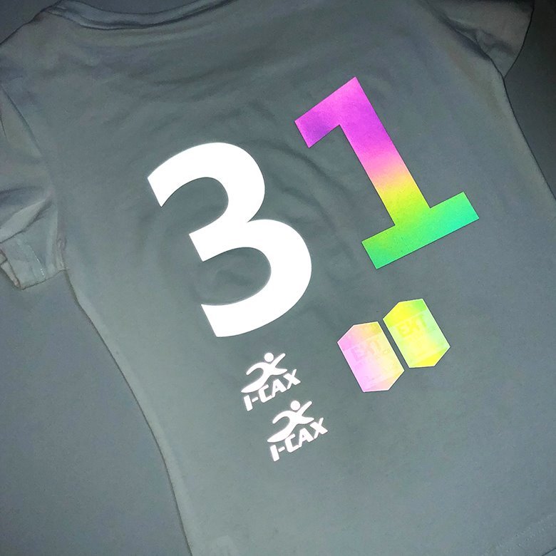 A detailed view of a reflective logo being heat-transferred onto a t-shirt, similar in finish to screen printing.